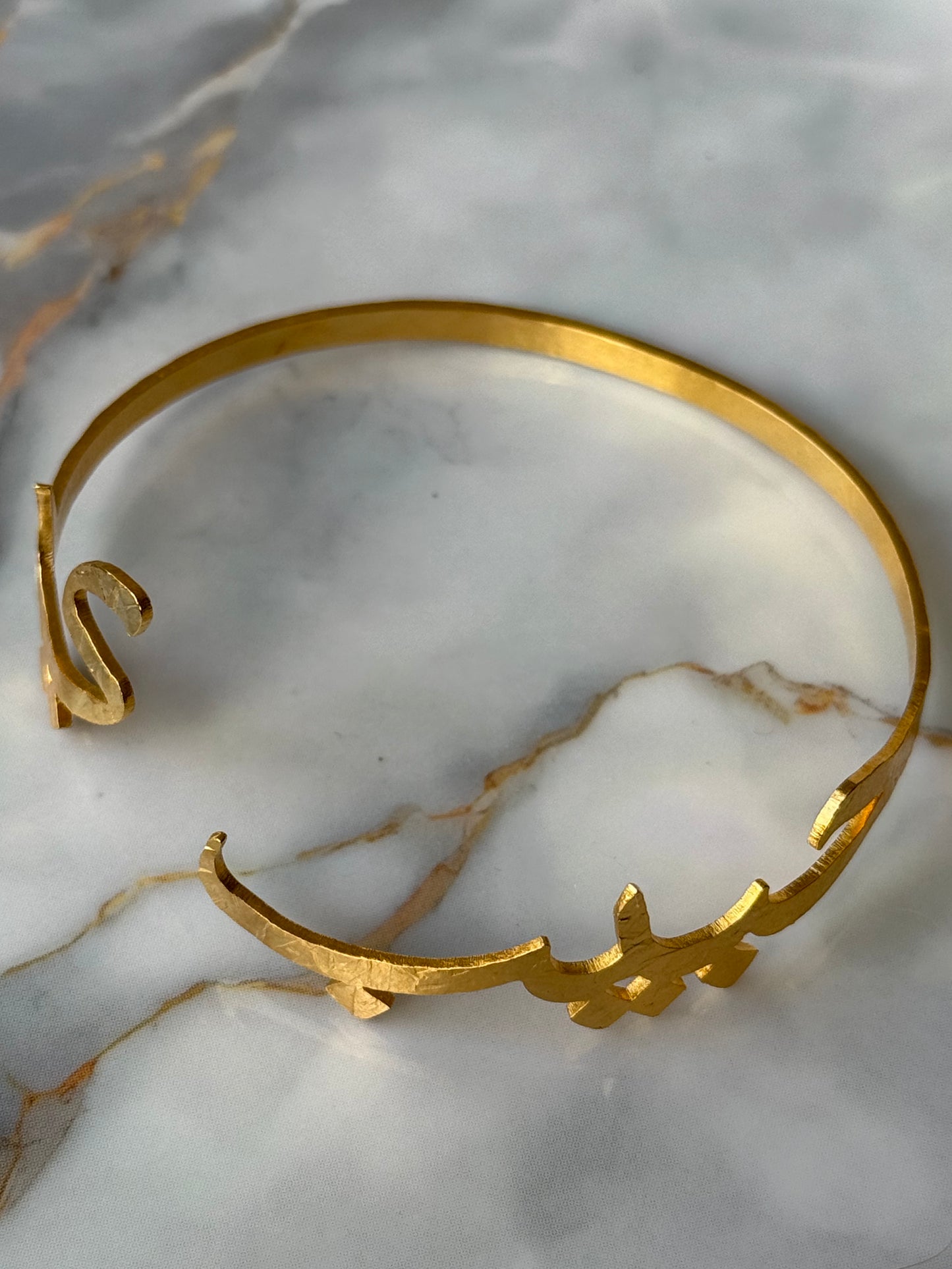 Gold-plated Arabic calligraphy bangle with the word “Habibi” (حبيبي), meaning My Sweetheart, artisan-crafted and ethically made for Suzy’s Treasures, displayed on a marble background.