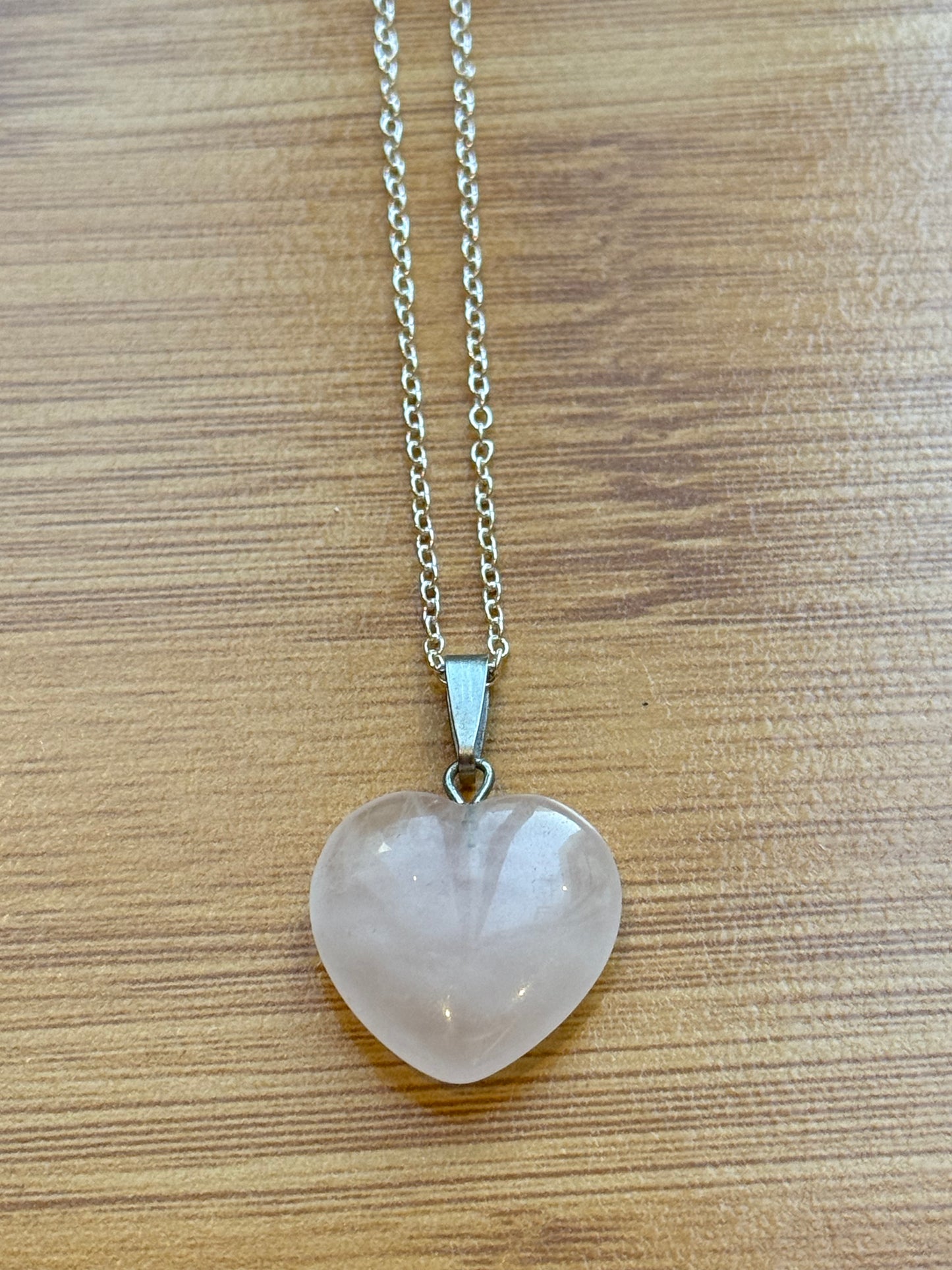 Rose Quartz heart-shaped pendant on sterling silver chain, placed on a wooden background β Suzys Treasures