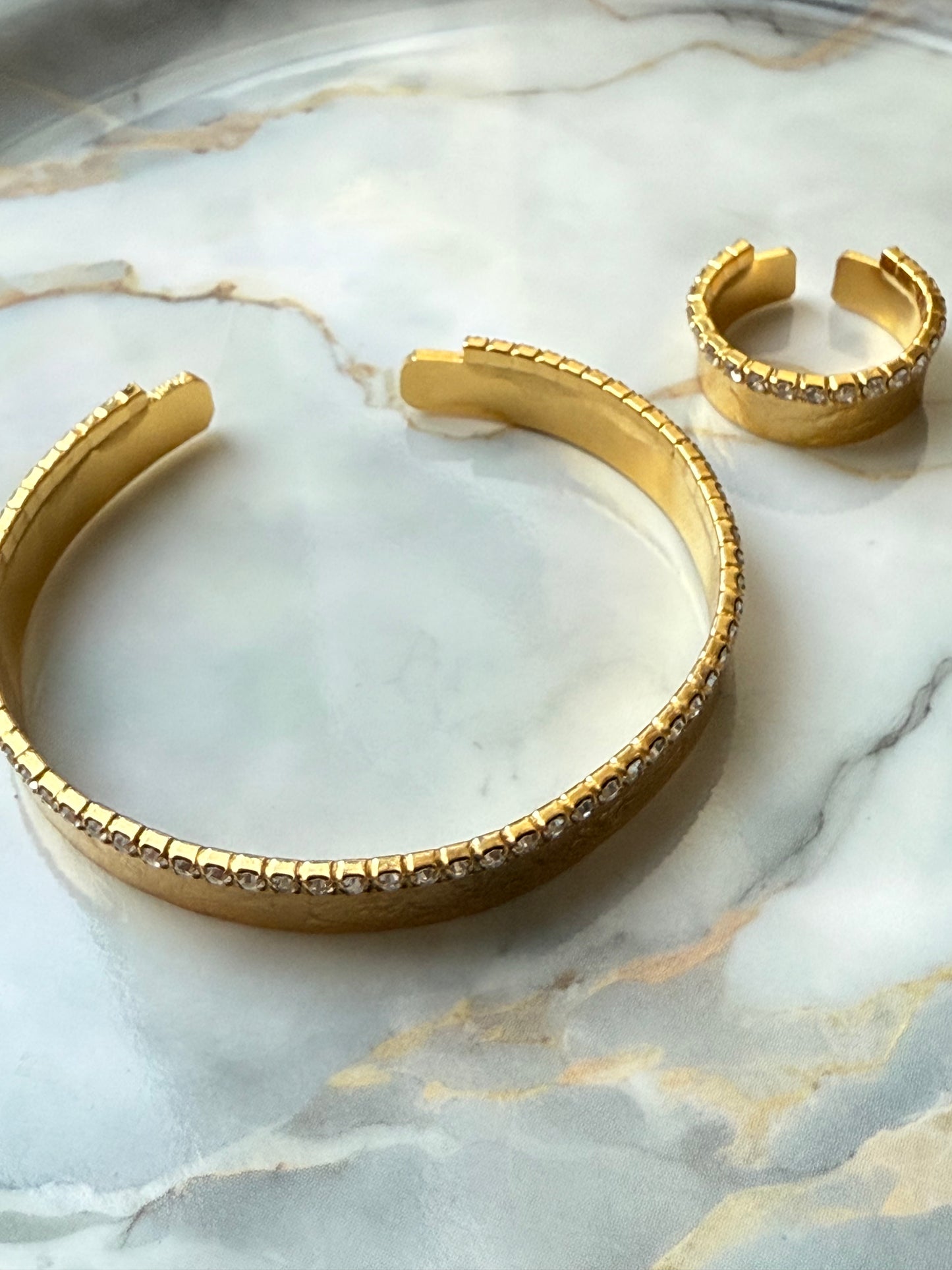 Gold-plated bangle and adjustable ring set featuring a single row of clear zirconia crystals, designed with minimalist elegance and handcrafted for Suzys Treasures, displayed on a marble background.