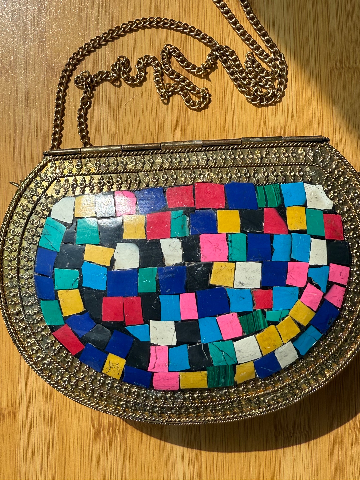 Colorful mosaic-patterned handbag with a chain on a wooden surface
