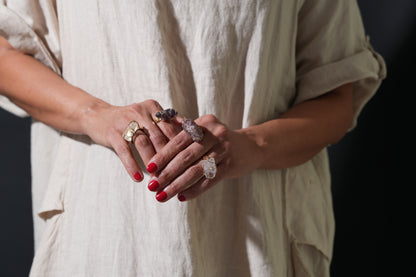 Woman wearing a collection of raw crystal gold-plated rings on both hands, featuring amethyst, strawberry and rose quartz – Suzys Treasures.