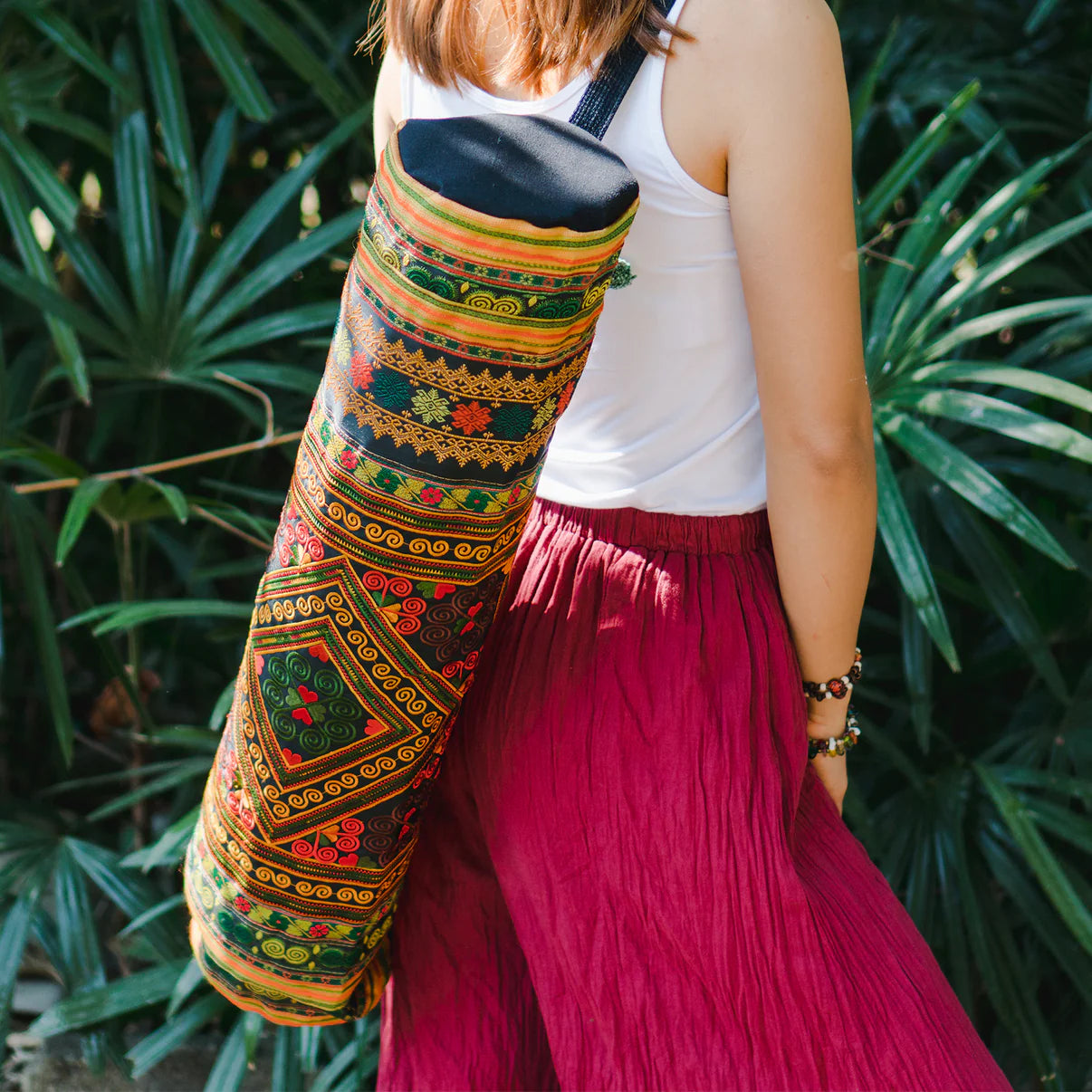 Woman carrying a colorful boho yoga bag with traditional ethnic patterns over her shoulder, standing outdoors surrounded by lush greenery – Suzys Treasures.