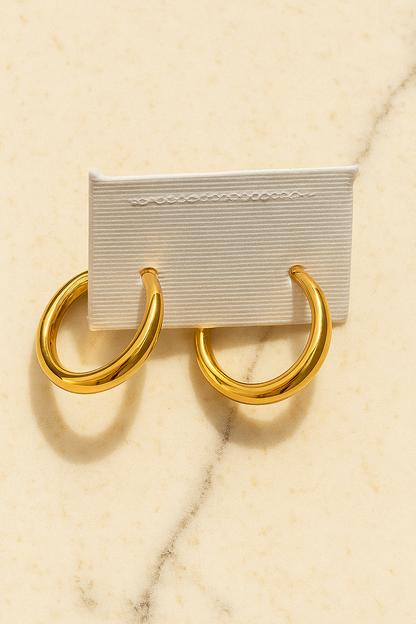 Gold hoop earrings on a white card against a beige marble background