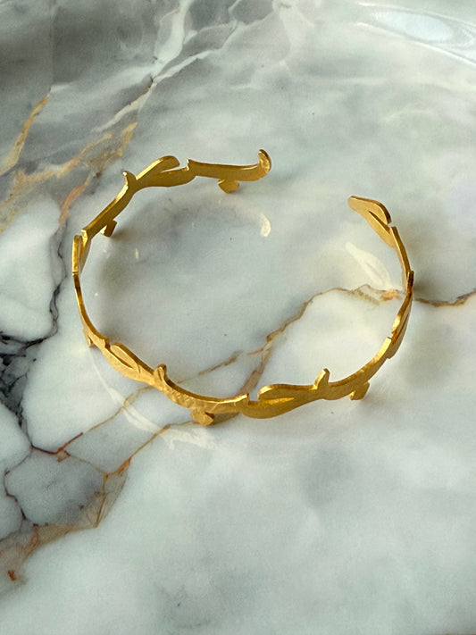 Gold-plated Arabic bangle with the word “Hub” (Love) in calligraphy, resting on a marble surface. Available at Suzy’s treasures online store. 