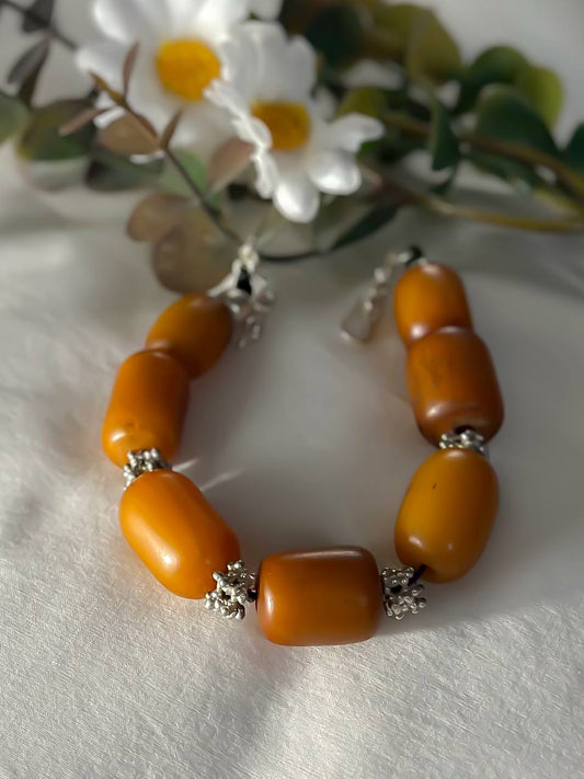 Suzys Treasures handcrafted Yemeni Amber & Silver Bracelet with warm honey-toned resin beads and silver accents, styled beside white daisies on a soft white fabric.