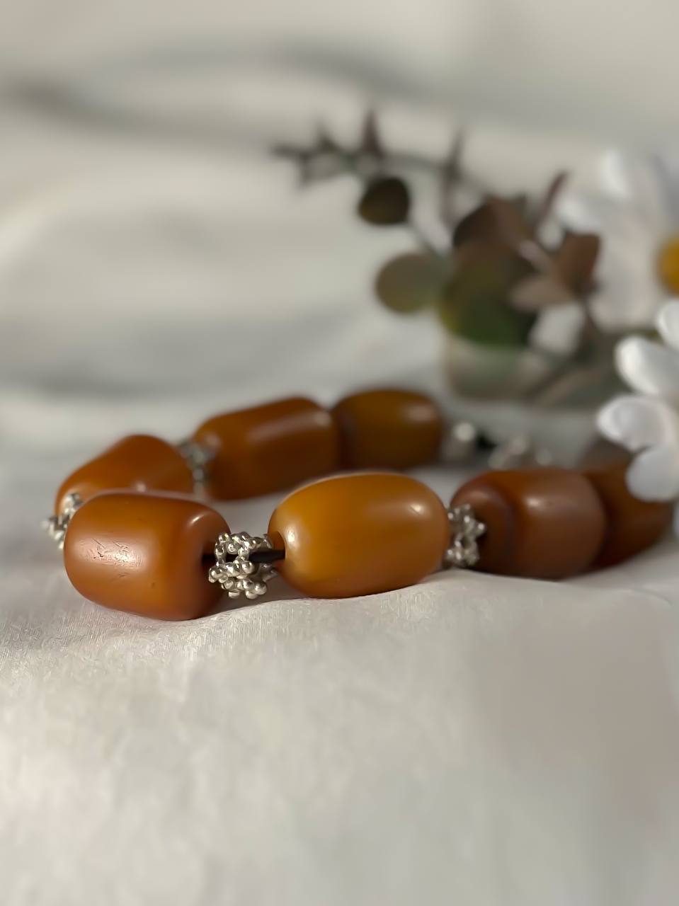 Suzys Treasures handcrafted Yemeni Amber & Silver Bracelet with warm honey-toned resin beads and silver accents, styled beside white daisies on a soft white fabric.