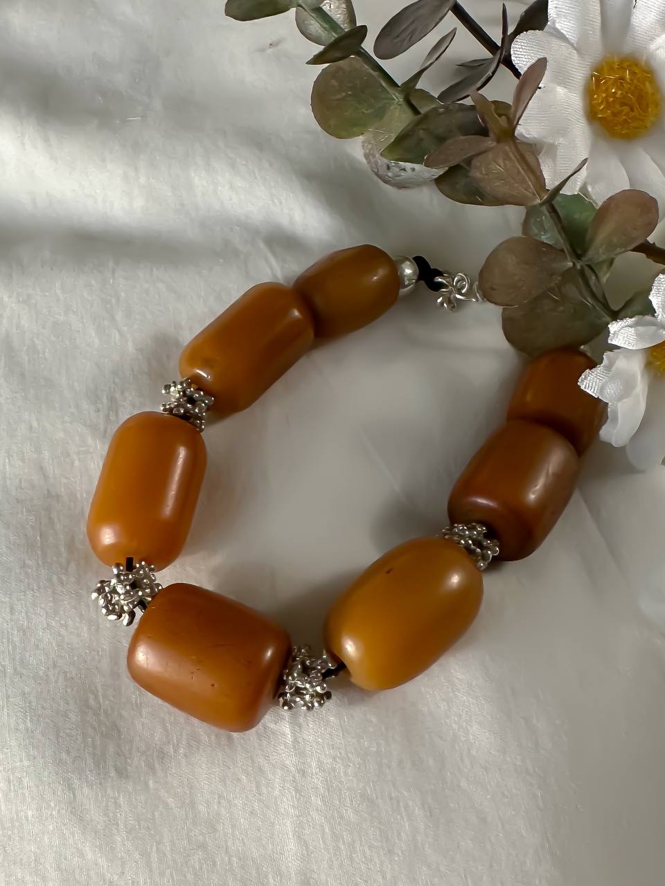 Suzys Treasures handcrafted Yemeni Amber & Silver Bracelet with warm honey-toned resin beads and silver accents, styled beside white daisies on a soft white fabric.