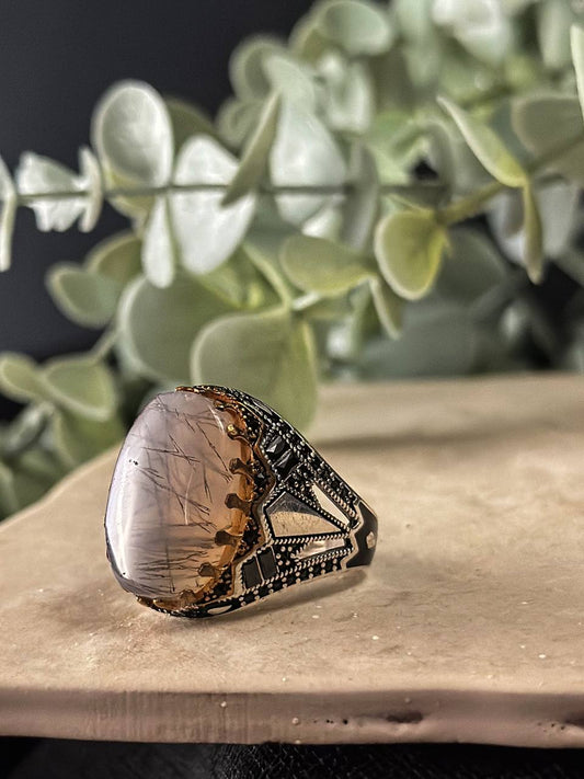 Suzys Treasures handcrafted Yemeni men’s ring featuring a Aqeeq (agate) stone set in an ornate sterling silver band with traditional motifs, displayed on a stone surface with a green leafy background.