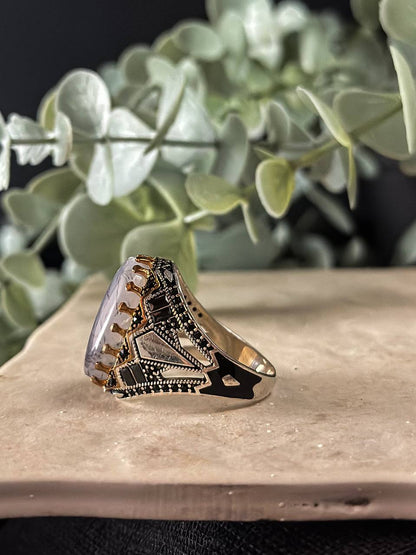 Suzys Treasures handcrafted Yemeni men’s ring featuring a Aqeeq (agate) stone set in an ornate sterling silver band with traditional motifs, displayed on a stone surface with a green leafy background.