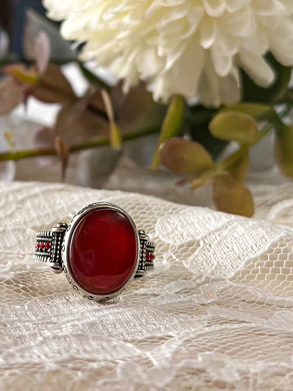 Suzys Treasures women's Yemeni Aqeeq ring featuring a deep red agate stone set in a detailed sterling silver band, displayed on lace fabric with a soft floral background.