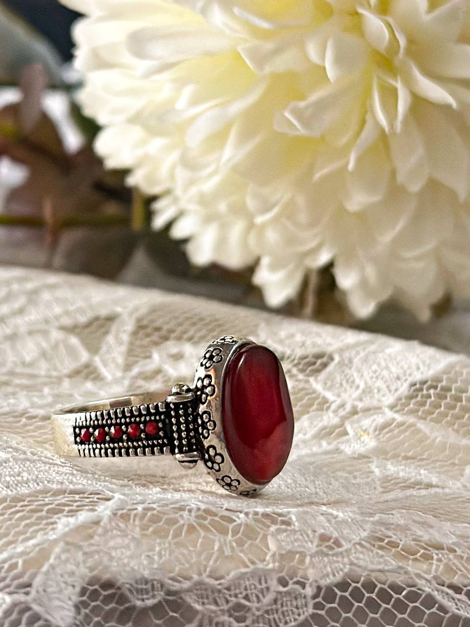 Suzys Treasures women's Yemeni Aqeeq ring featuring a deep red agate stone set in a detailed sterling silver band, displayed on lace fabric with a soft floral background.