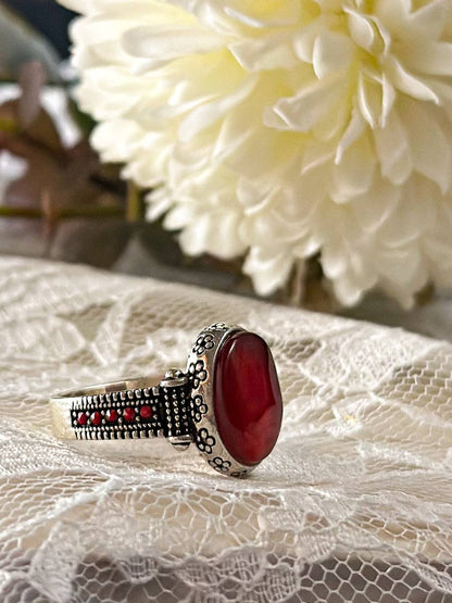 Suzys Treasures women's Yemeni Aqeeq ring featuring a deep red agate stone set in a detailed sterling silver band, displayed on lace fabric with a soft floral background.