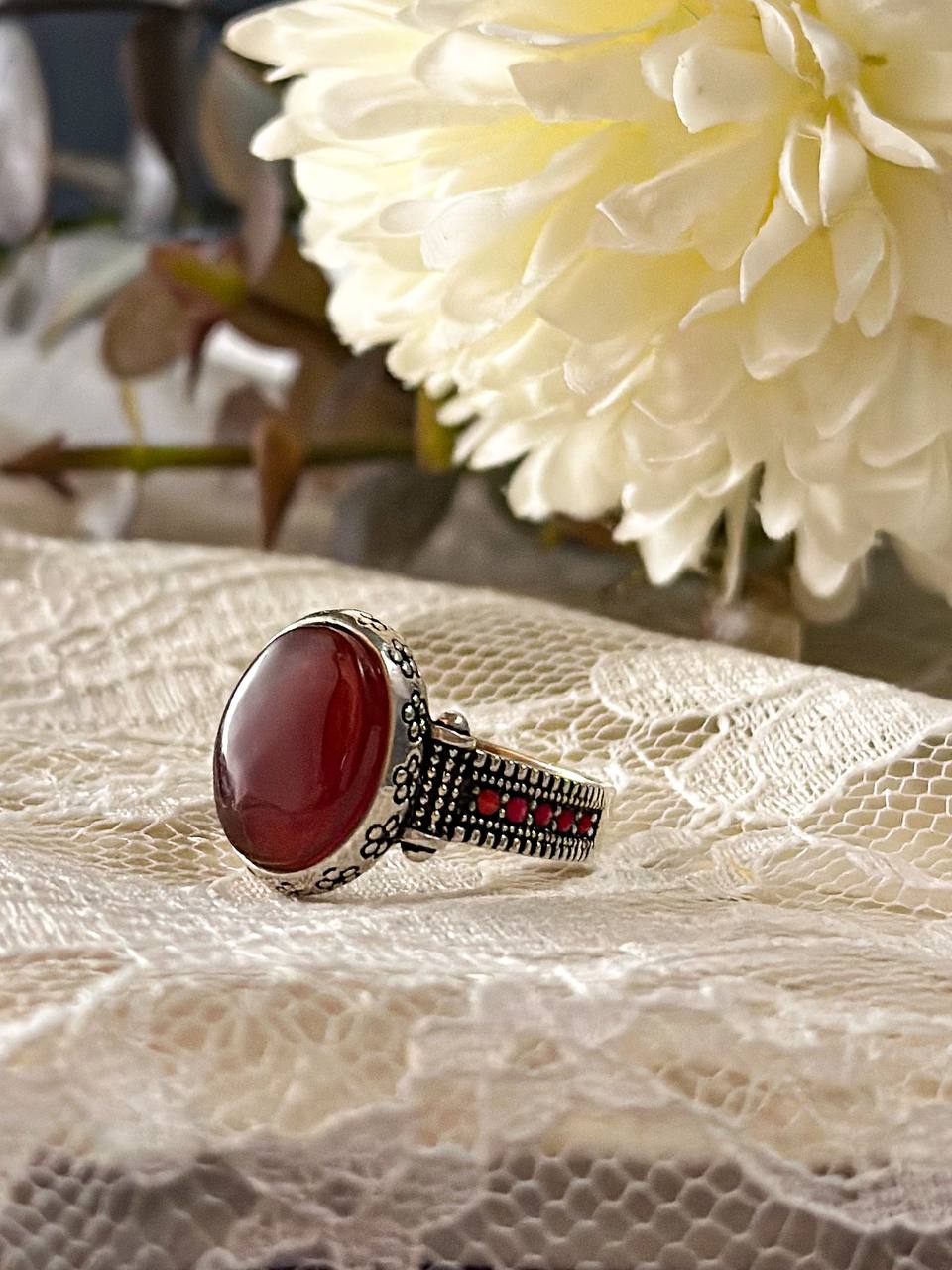 Suzys Treasures women's Yemeni Aqeeq ring featuring a deep red agate stone set in a detailed sterling silver band, displayed on lace fabric with a soft floral background.