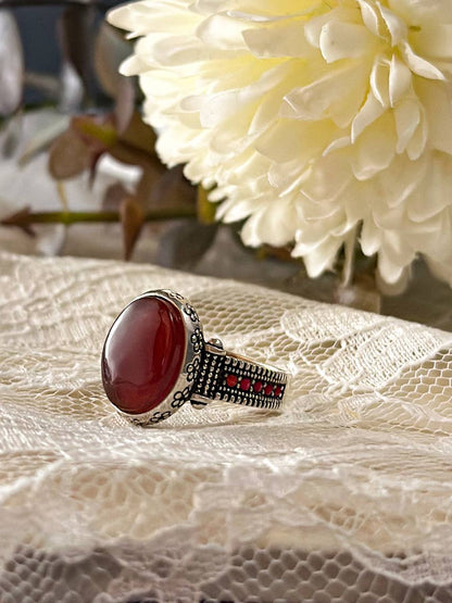Suzys Treasures women's Yemeni Aqeeq ring featuring a deep red agate stone set in a detailed sterling silver band, displayed on lace fabric with a soft floral background.