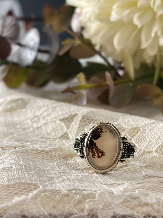 Suzys Treasures women's Yemeni dendritic agate ring with a detailed sterling silver band, displayed on delicate lace fabric with soft floral background.