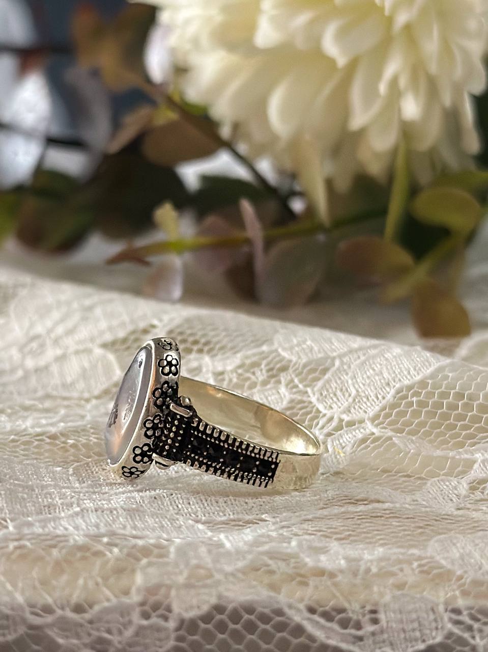 Suzys Treasures women's Yemeni dendritic agate ring with a detailed sterling silver band, displayed on delicate lace fabric with soft floral background.