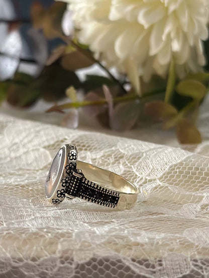 Suzys Treasures women's Yemeni dendritic agate ring with a detailed sterling silver band, displayed on delicate lace fabric with soft floral background.