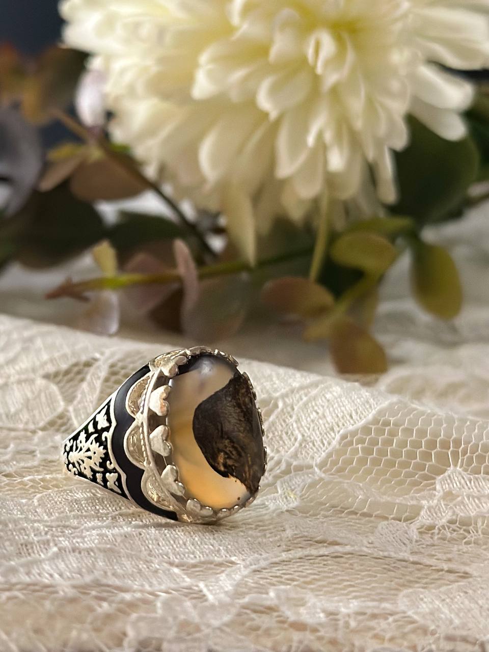 Suzys Treasures women's Yemeni dendritic agate ring with a bold organic pattern set in sterling silver, displayed on delicate lace fabric with soft floral background.