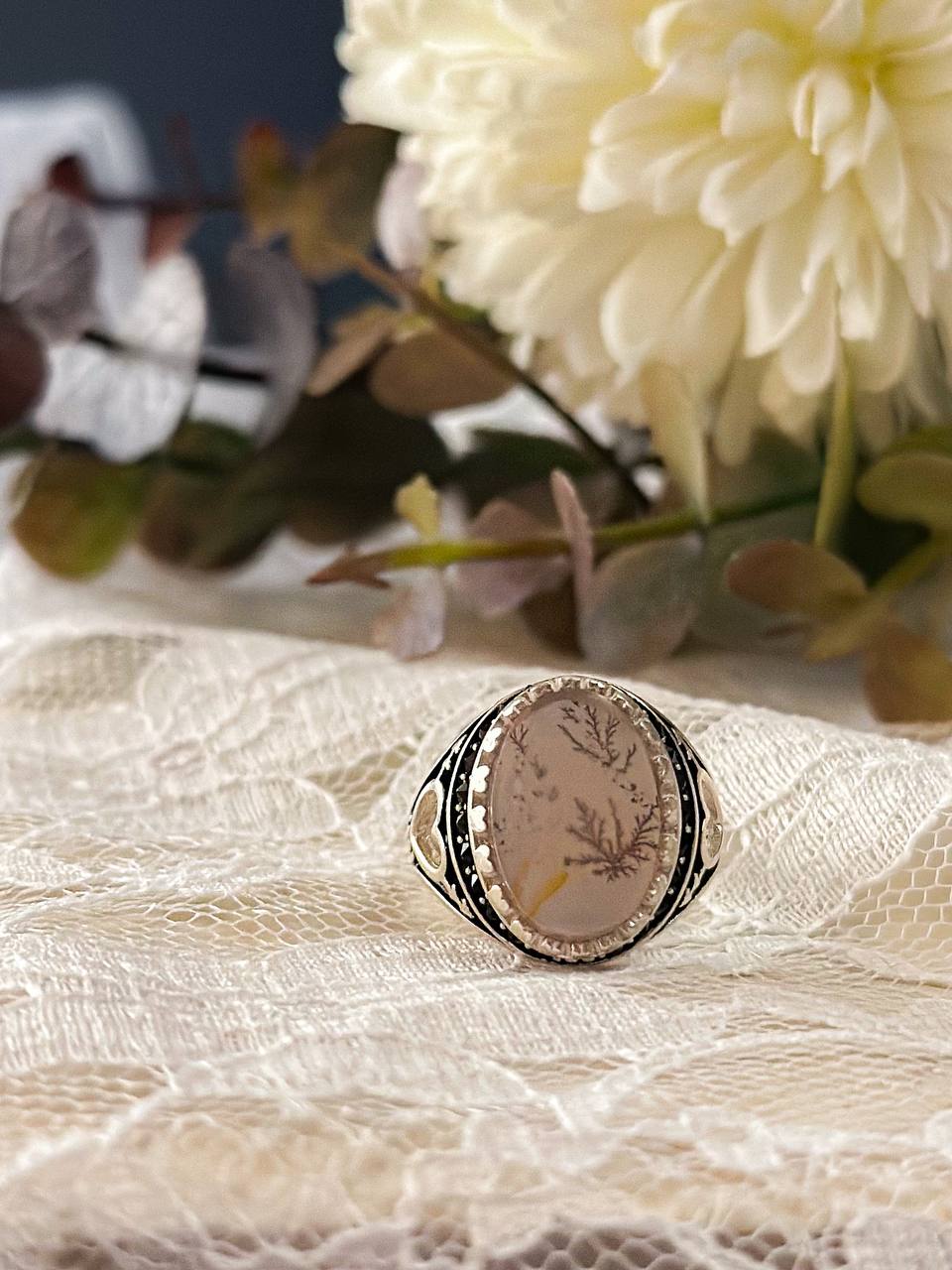 Suzys Treasures handcrafted Yemeni dendritic agate sterling silver ring, symbolizing growth and elegance, displayed on lace fabric with soft floral background.