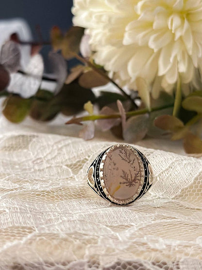 Suzys Treasures handcrafted Yemeni dendritic agate sterling silver ring, symbolizing growth and elegance, displayed on lace fabric with soft floral background.
