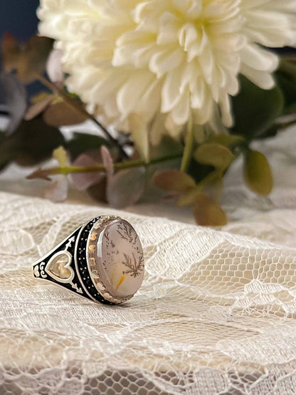 Suzys Treasures handcrafted Yemeni dendritic agate sterling silver ring, symbolizing growth and elegance, displayed on lace fabric with soft floral background.