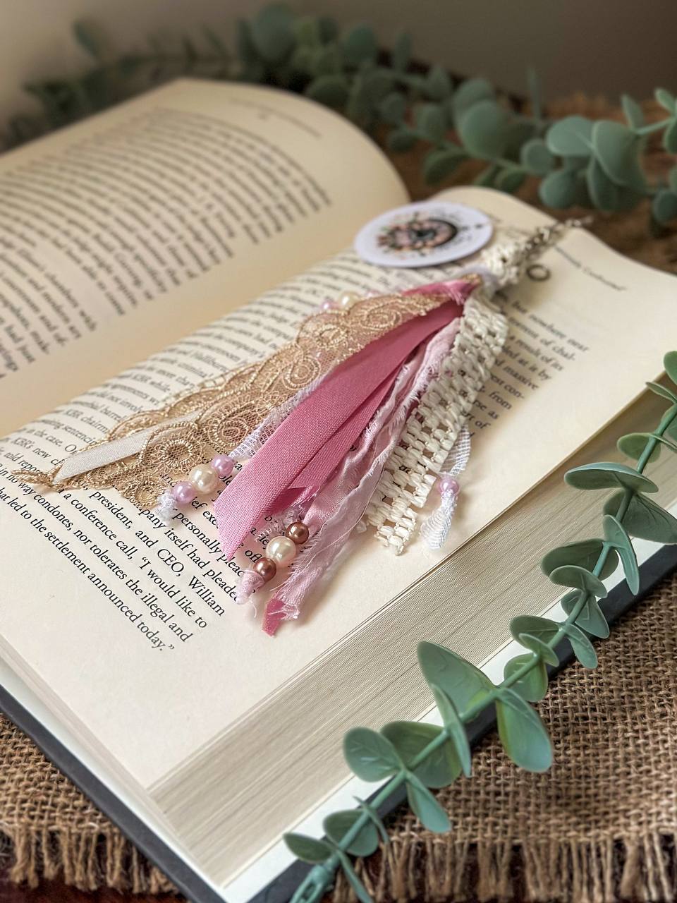 Handmade Boho tassel paperclip bookmark from Suzys Treasures, featuring pink and white lace ribbons, pearl bead accents, and crochet trim, displayed on an open book – a charming and versatile accessory for journals, planners, or novels.