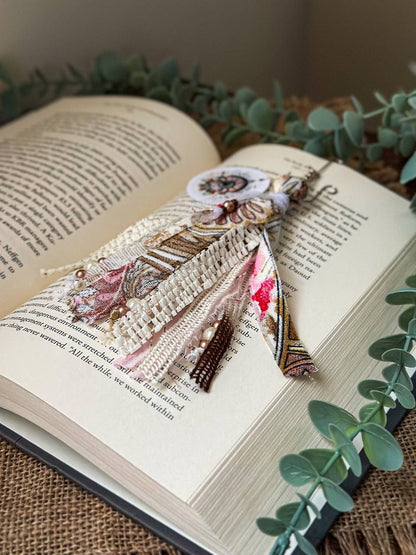 Handmade Boho tassel paperclip bookmark from Suzys Treasures, featuring pink and white lace ribbons, pearl bead accents, and crochet trim, displayed on an open book – a charming and versatile accessory for journals, planners, or novels.