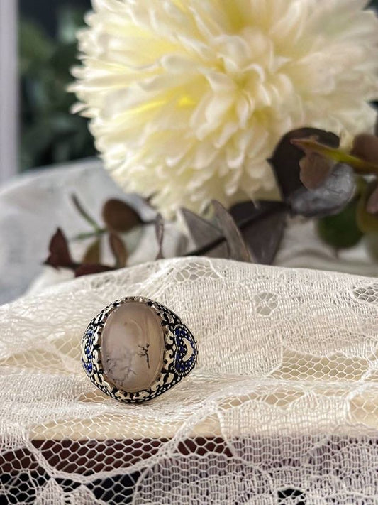 Suzys Treasures women's Yemeni dendritic agate ring with intricate silver and blue enamel detailing, set against lace fabric with a soft floral background.
