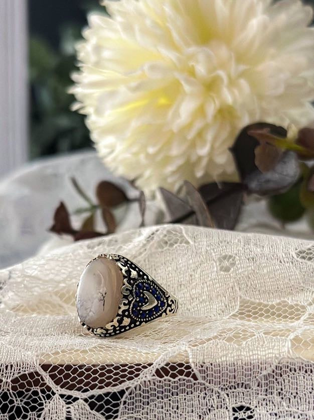 Suzys Treasures women's Yemeni dendritic agate ring with intricate silver and blue enamel detailing, set against lace fabric with a soft floral background.