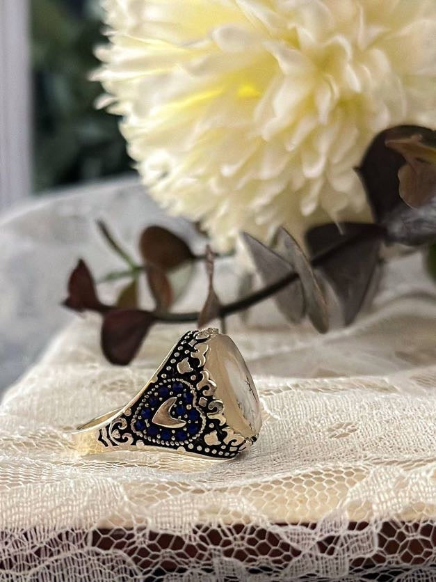 Suzys Treasures women's Yemeni dendritic agate ring with intricate silver and blue enamel detailing, set against lace fabric with a soft floral background.