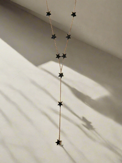 Close-up of Suzys Treasures necklace with black hematite star charms on a silver embossed, warm-toned 3-micron plated chain, displayed on a light beige surface with natural shadows.