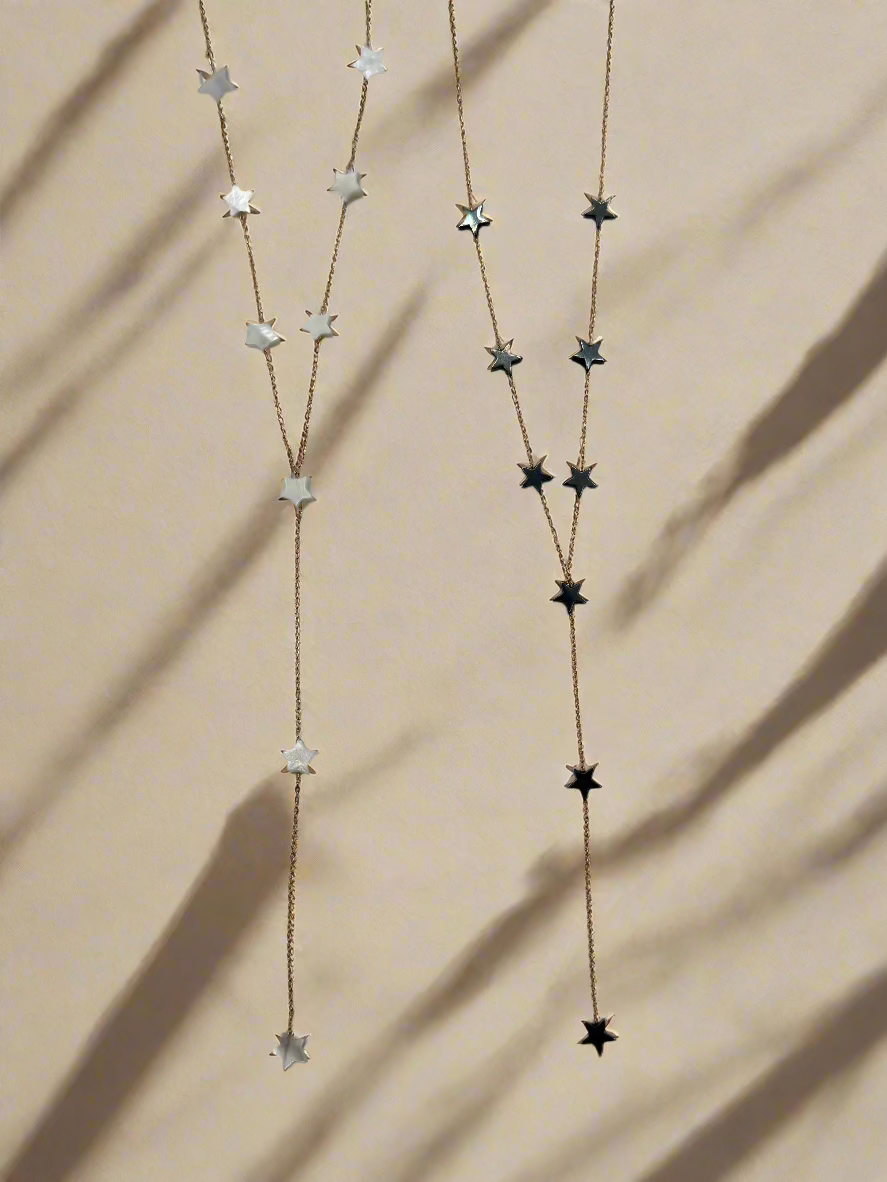 Suzys Treasures handcrafted necklaces featuring mother of pearl stars and black hematite stars on silver embossed, warm-toned 3-micron plated chains, displayed on a beige background with soft shadows."