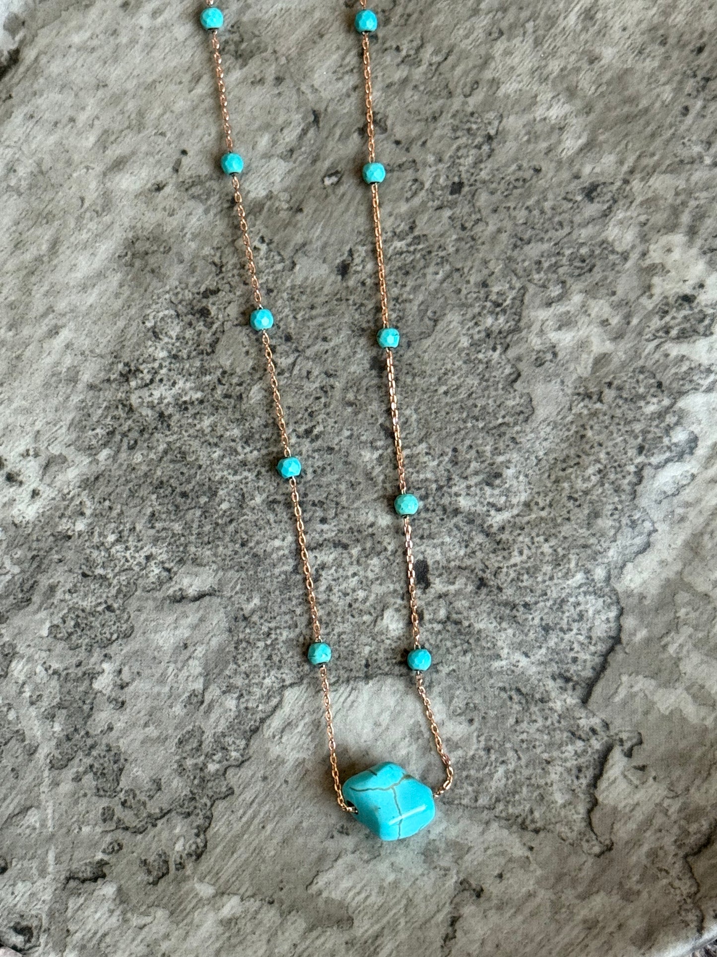 Suzys Treasures handcrafted short necklace with a turquoise gemstone on a silver embossed, warm-toned 3-micron plated chain, displayed on a textured stone background.
