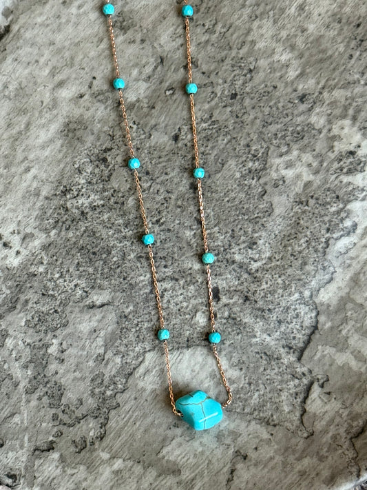 Suzys Treasures handcrafted short necklace with a turquoise gemstone on a silver embossed, warm-toned 3-micron plated chain, displayed on a textured stone background.