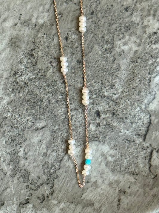 Suzys Treasures handcrafted short necklace with clusters of freshwater pearls and a single turquoise bead on a silver embossed, 3-micron plated chain, displayed on a textured stone background.