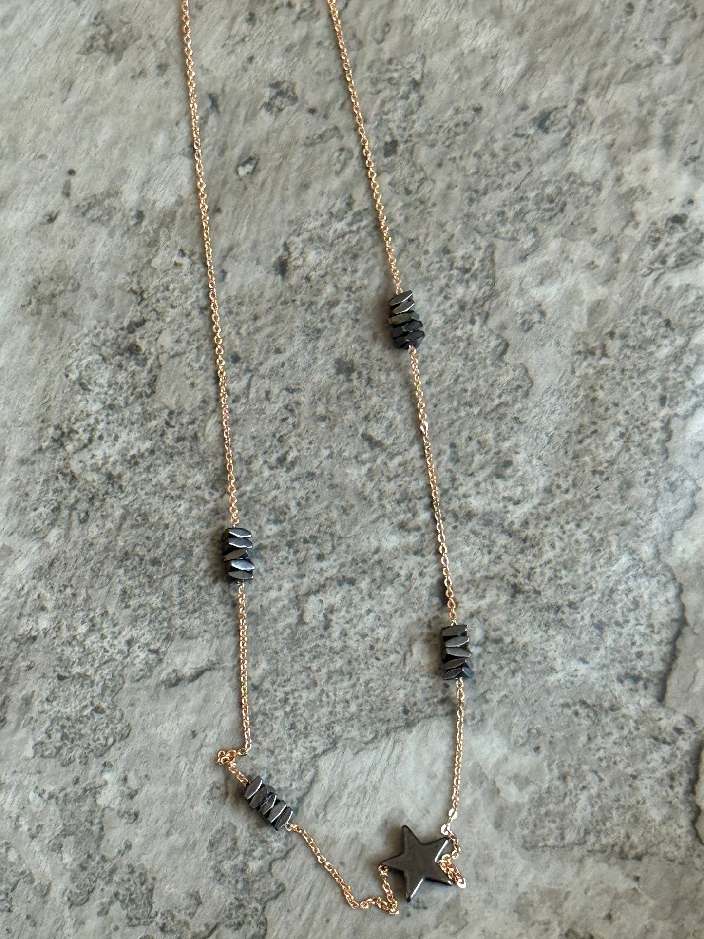 Suzys Treasures handcrafted short necklace featuring stacked grey hematite beads and a hematite star charm on a silver embossed, warm-toned 3-micron plated chain, displayed on a textured stone background.