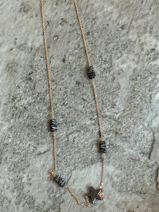 Suzys Treasures handcrafted short necklace featuring stacked grey hematite beads and a hematite star charm on a silver embossed, warm-toned 3-micron plated chain, displayed on a textured stone background.