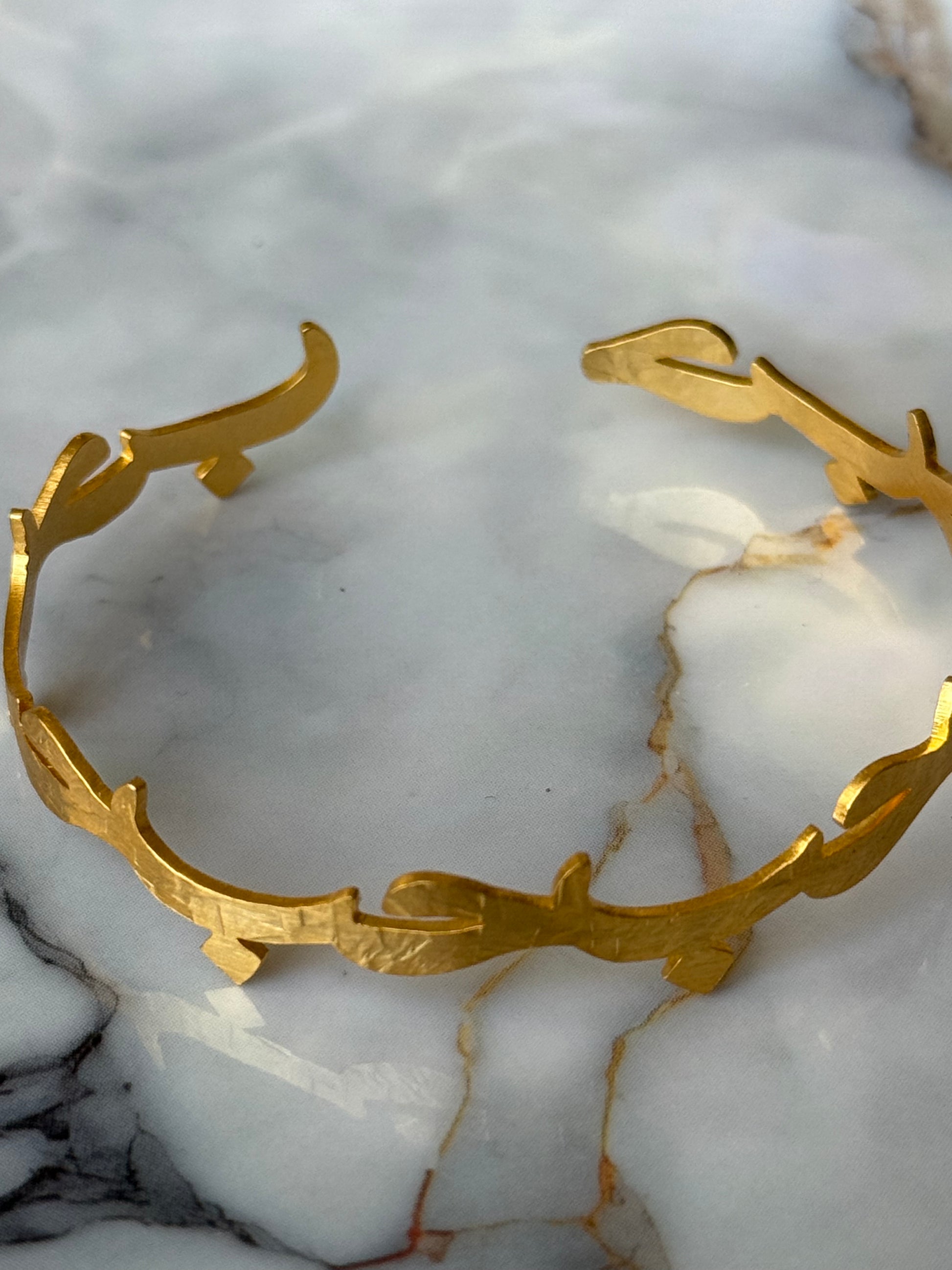 Gold-plated Arabic bangle with the word “Hub” (Love) in calligraphy, resting on a marble surface. Available at Suzy’s treasures online store. 