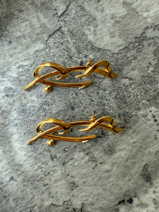Gold-plated sculptural earrings shaped in flowing Arabic calligraphy spelling “Hob” (حب), meaning love, handcrafted for Suzys Treasures and displayed on a textured stone background.
