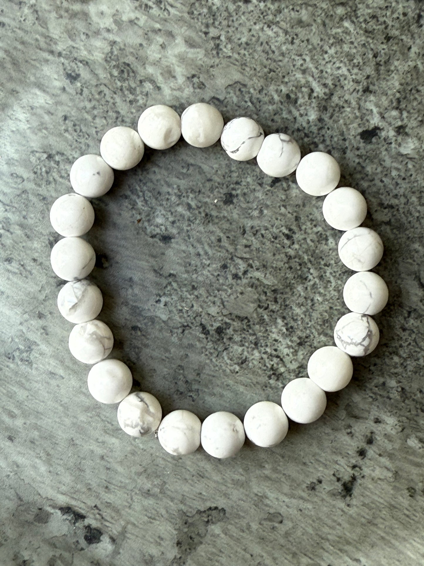 Howlite round bead bracelet with white and grey marbled stones, displayed on a stone background — crystal jewelry from Suzys Treasures.