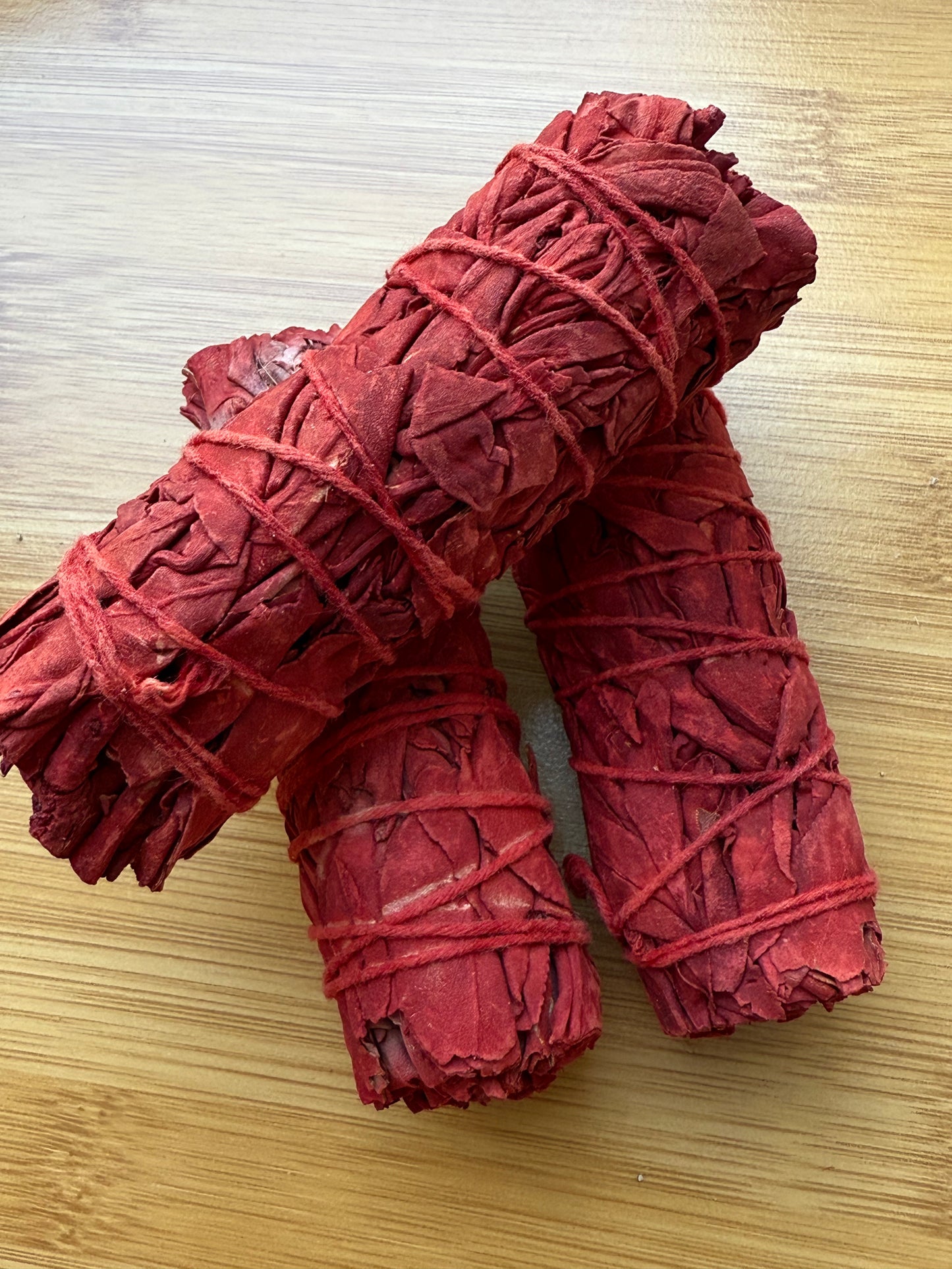 Bright red Dragon’s Blood sage smudge sticks wrapped in red string, placed on a wooden surface, used for energy cleansing and spiritual rituals, available at Suzy’s Treasures.