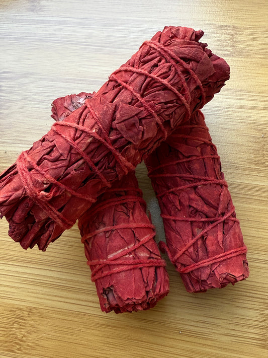 Bright red Dragon’s Blood sage smudge sticks wrapped in red string, placed on a wooden surface, used for energy cleansing and spiritual rituals, available at Suzy’s Treasures.
