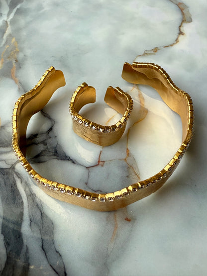 Gold-plated copper bangle and adjustable ring set with a wavy-edge design and a single row of clear zirconia crystals, handcrafted for Suzy’s Treasures and displayed on a marble background.