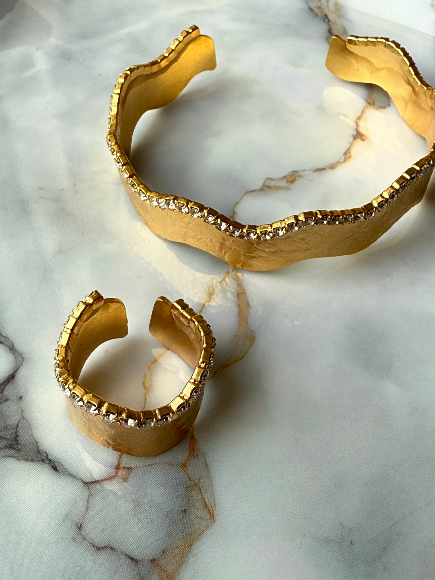 Gold-plated copper bangle and adjustable ring set with a wavy-edge design and a single row of clear zirconia crystals, handcrafted for Suzys Treasures and displayed on a marble background.