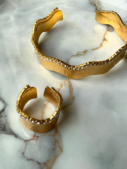 Gold-plated copper bangle and adjustable ring set with a wavy-edge design and a single row of clear zirconia crystals, handcrafted for Suzys Treasures and displayed on a marble background.