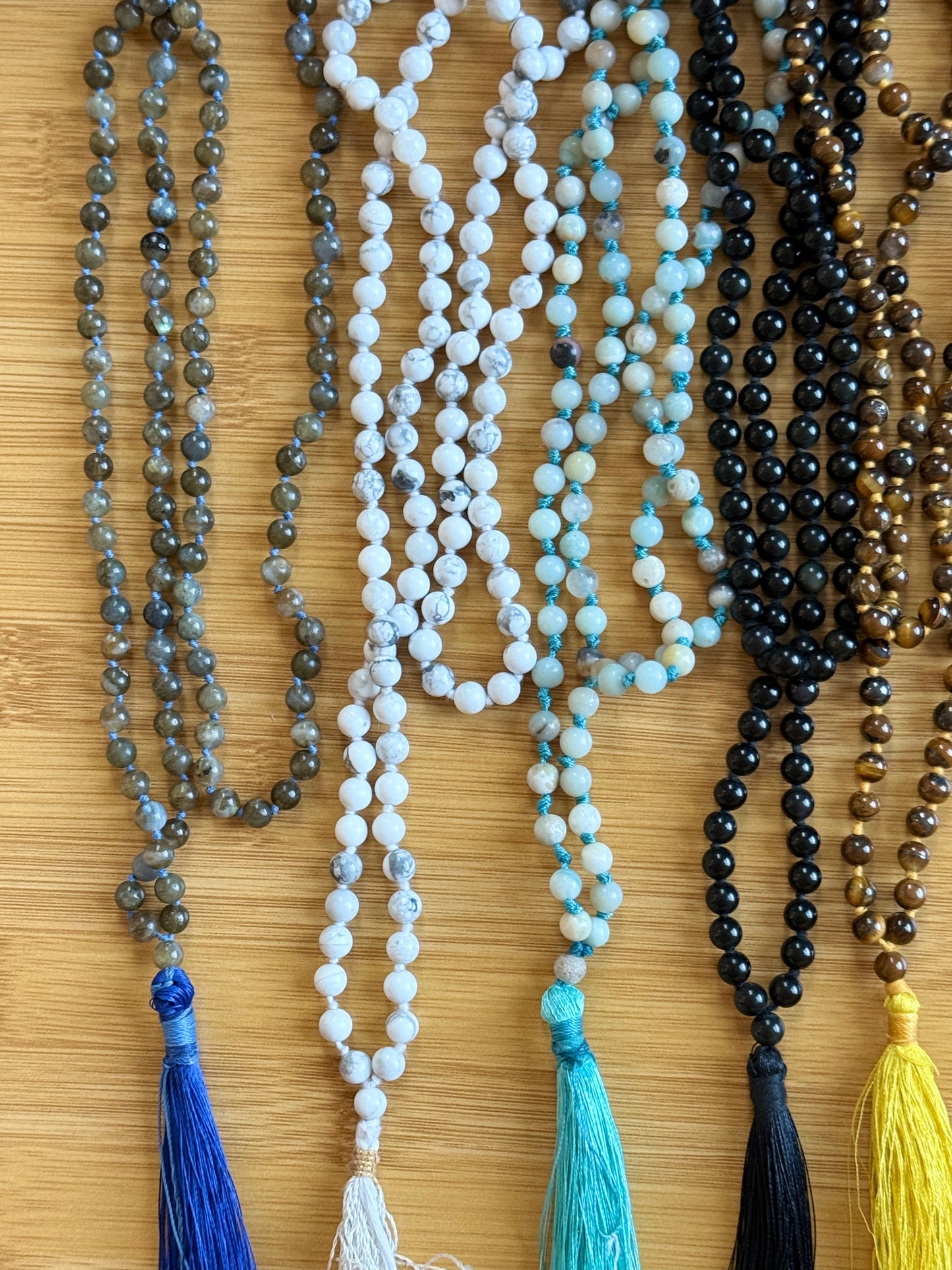 Assorted 108-bead crystal mala necklaces with 6mm round beads in natural stones like Labradorite, Howlite, Amazonite, Black Onyx, and Tiger Eye, handmade with tassels, from the Crystal Jewelry collection at Suzys Treasures.