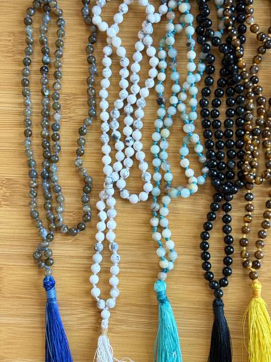 Assorted 108-bead crystal mala necklaces with 6mm round beads in natural stones like Labradorite, Howlite, Amazonite, Black Onyx, and Tiger Eye, handmade with tassels, from the Crystal Jewelry collection at Suzys Treasures.
