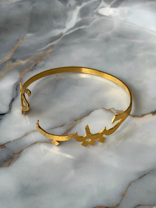 Gold-plated Arabic calligraphy bangle with the word “Habibi” (حبيبي), meaning My Sweetheart, artisan-crafted and ethically made for Suzy’s Treasures, displayed on a marble background.

