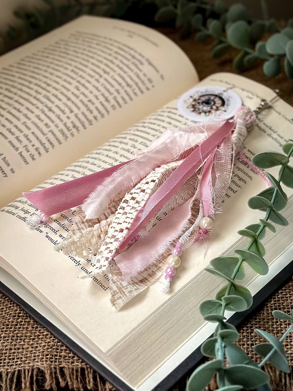 Handmade Boho tassel paperclip bookmark from Suzys Treasures, featuring pink and white  lace ribbons, pearl bead accents, and crochet trim, displayed on an open book – a charming and versatile accessory for journals, planners, or novels.