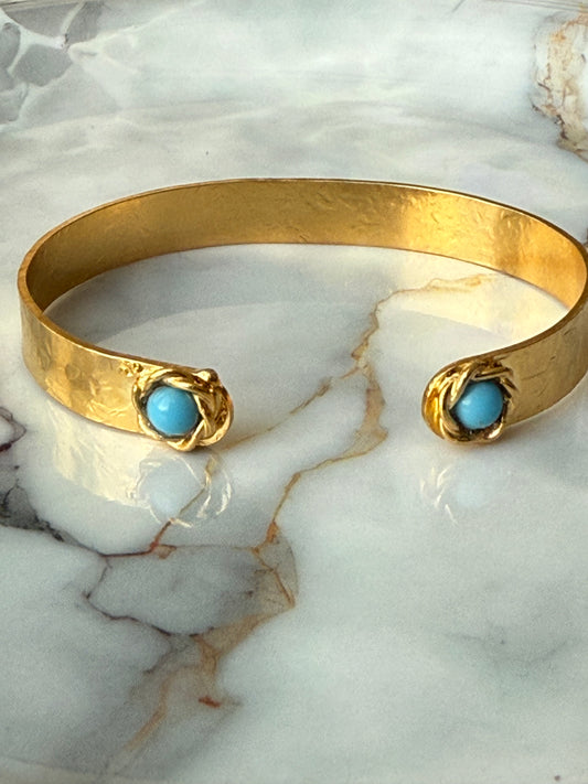 Gold-plated bangle with black Murano glass evil eyes, artisan-crafted and symbolizing protection, available at Suzy’s Treasures, photographed on a marble background.

